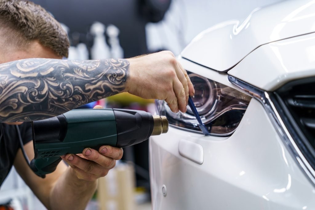 Sticker of a protective film on the headlight of a car in a car detailing studio
